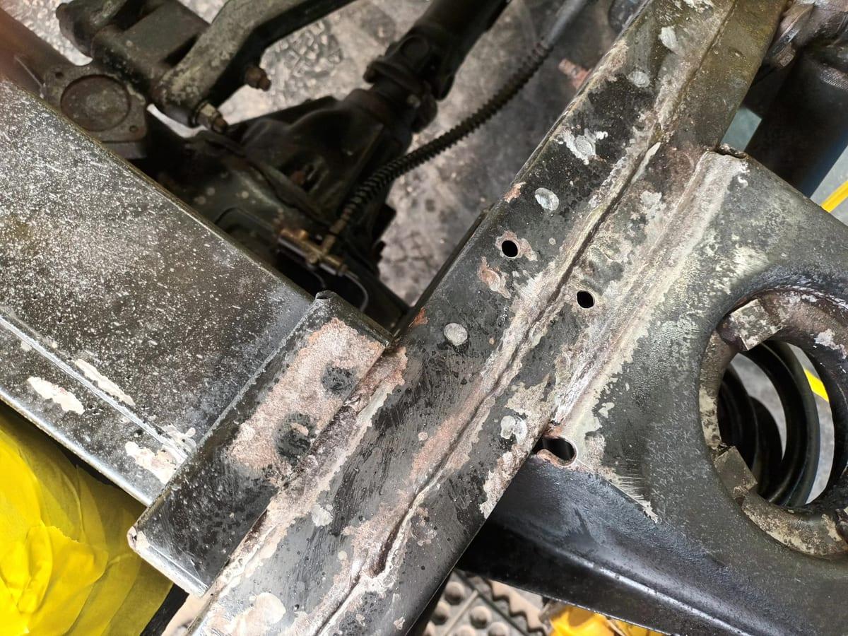 Pale chalky iron phosphate across a Defender chassis rail where the rust converter has reacted