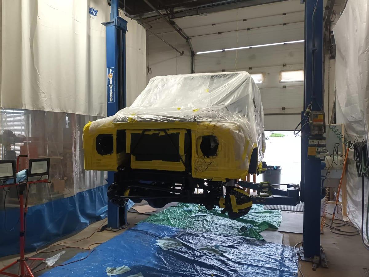 Defender on the hoist with the body sheeted and panels masked before coating