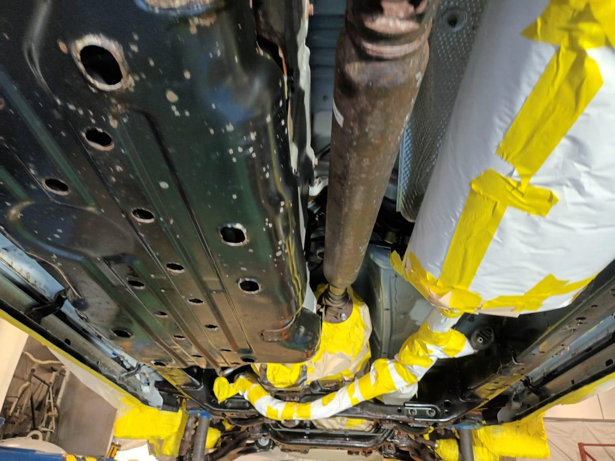 Masked fuel tank and driveshaft on a 4Runner, with pale rust converter spots across the floor pan